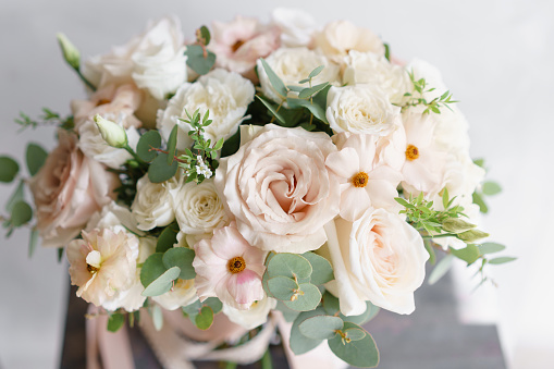 Wedding bouquet of white roses and buttercup on a wooden table. Lots of greenery, modern asymmetrical disheveled bridal bunch. Pastel color