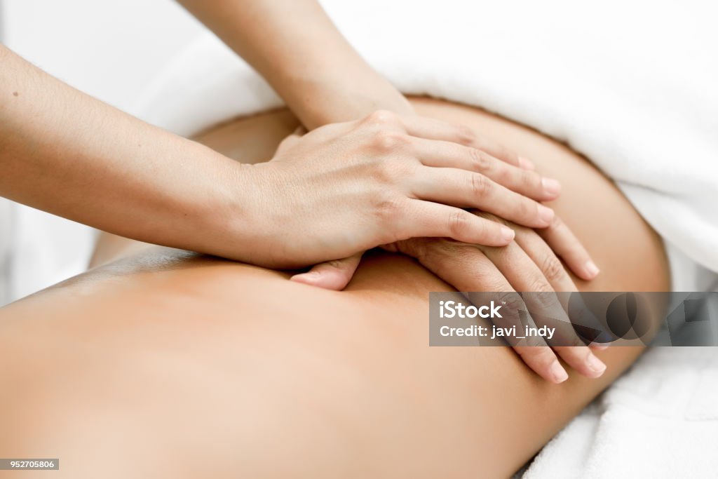 Young woman receiving a back massage in a spa center. Young woman receiving a back massage in a spa center. Female patient is receiving treatment by professional therapist. Massaging Stock Photo