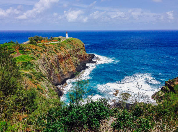A view of blue ocean water and the Kilauea Lighthouse in Kaua'i Blue ocean water and lush vegetation surround Kilauea Lighthouse, located on the North Shore of Kaua'i, Hawaii. kīlauea volcano photos stock pictures, royalty-free photos & images