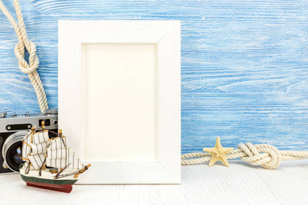 empty photo frame on blue wooden background with starfish, ship, marine knots, classic camera. summer holiday concept
