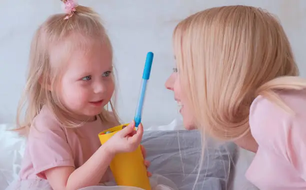 Young attractive blond woman kiss her little charming daughter in pink dresses with felt-pens.