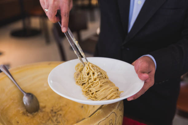 Chef neatly plating spaghetti carbonara in cheese wheel on white plate.