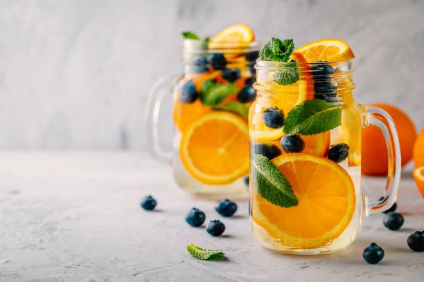 Infused detox water with orange, blueberry and mint. Ice cold summer cocktail or lemonade. Infused detox water with orange, blueberry and mint. Ice cold summer cocktail or lemonade in glass mason jar infused water stock pictures, royalty-free photos & images