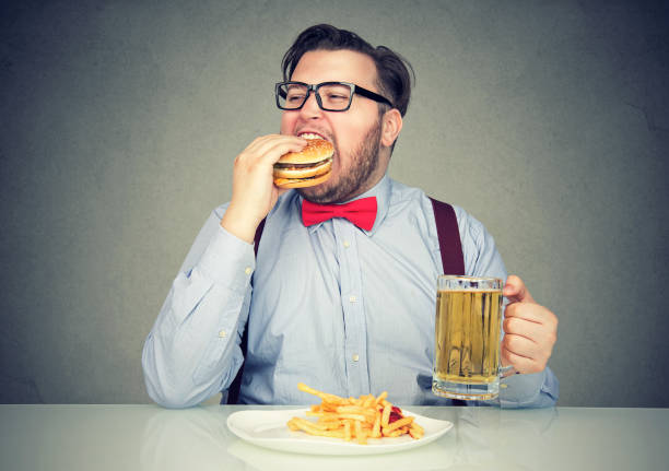 uomo che mangia cibo spazzatura bevendo birra - chaos foto e immagini stock