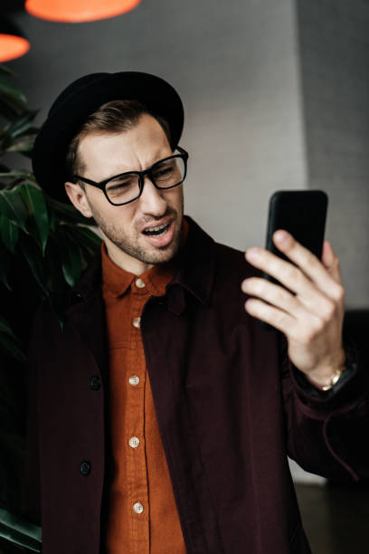 istock handsome stressed man in hat and glasses looking at smartphone 952767970