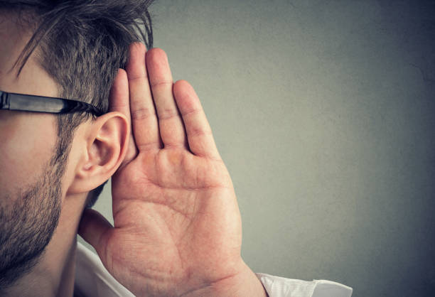 hombre sostiene su mano junto a la oreja y escucha atentamente - entrometido fotografías e imágenes de stock