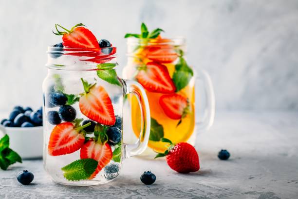 Infused detox water with blueberry, strawberry, orange and mint. Ice cold summer cocktail or lemonade. Infused detox water with blueberry, strawberry, orange and mint. Ice cold summer cocktail or lemonade in glass mason jar infused water stock pictures, royalty-free photos & images