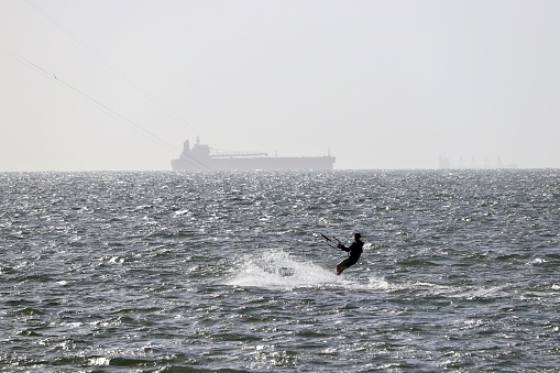 Wind surfer surfing in ocean with cargo ship in distance