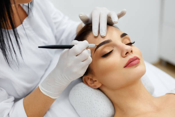 Beautician Doing Permanent Eyebrows Makeup Tattoo On Woman Face Permanent Makeup For Eyebrows. Closeup Of Beautiful Woman With Thick Brows In Beauty Salon. Beautician Doing Eyebrow Tattooing For Female Face. Beauty Procedure. High Resolution beauty clinic stock pictures, royalty-free photos & images