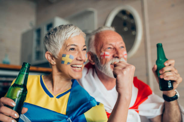 istock Mature couple watching soccer game and supporting different teams on TV 952779178