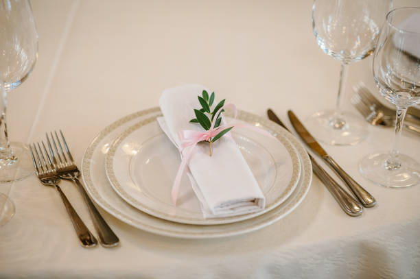 istock Serving, setting table. Two plates, glass glasses, silverware cutlery with linen napkin are decorated pink ribbons, branch greens. Wedding table decoration. Artwork. Close up. Side view. 952786592