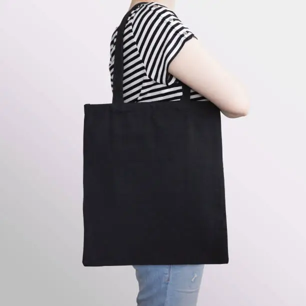 Girl is holding black cotton eco tote bag, design mockup. Handmade shopping bag for girls.