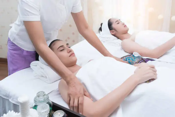 Photo of Beautiful young Asian woman relaxing , lying on massage table and having Thai traditional massage in spa salon