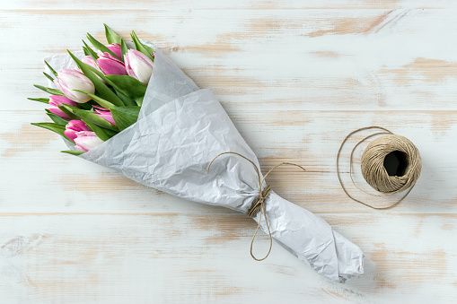 Pink tulips wrapped in white paper on wooden background. Flat lay. Love concept.