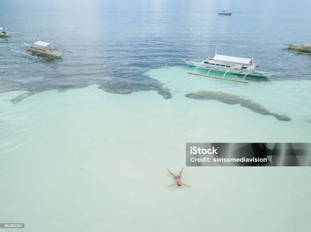 Aerial view of man relaxing in tropical sea like star shape, beach vacations concept Drone point of view aerial view of young man relaxing in the sea, tropical climate, white sand beach and turquoise water. People travel holiday concept. Shot in the Philippines 20-29 Years Stock Photo
