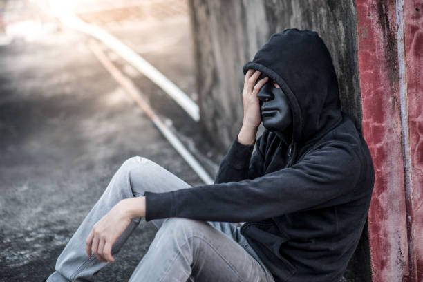 istock Mystery man with black mask in headache gesture feeling stressed and depressed while sitting near grunge concrete wall in abandoned building 952836964