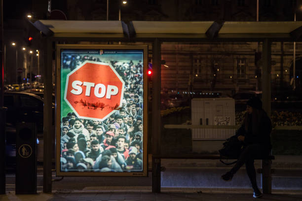 Anti Immigration poster from Viktor Orban government in the streets of Budapest during the 2018 general elections campaign Picture of a woman waiting at night at a bus stop next to a poster from Hungarian PM Viktor Orban against immigration, during the campaign for the 2018 parliament elections in Hungary populism stock pictures, royalty-free photos & images