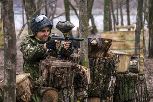 Paintball player takes aim, hides and shooting. Man wearing protective equipment