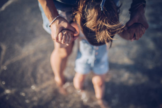 Holding hands, family or children with a mother and daughter outdoor together at the beach during summer. Kids, love or trust with a woman and female child standing outside for bonding during the day