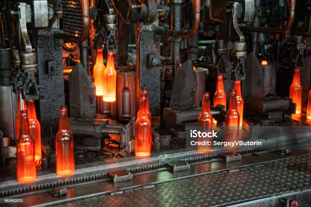 Plant for the production of bottles, glass plant Automated line for the production of glass containers. The hot bottles are put on a moving conveyor Glass - Material Stock Photo