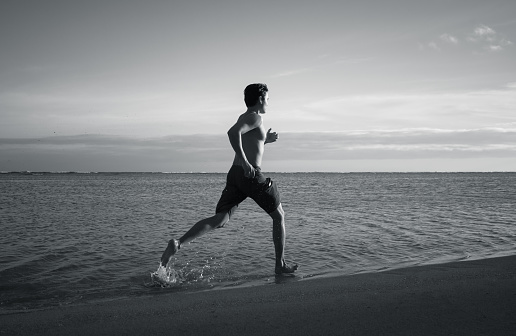 Black and white image of a male running on the beach. Location Hawaii.