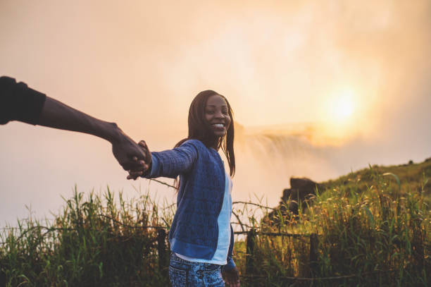 istock Holding hands looking at camera with Victoria Falls background 952965042