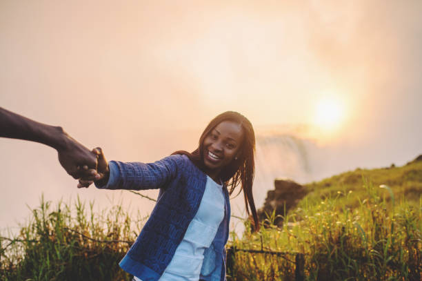 istock Holding hands with Victoria Falls background smiling at camera 952965290