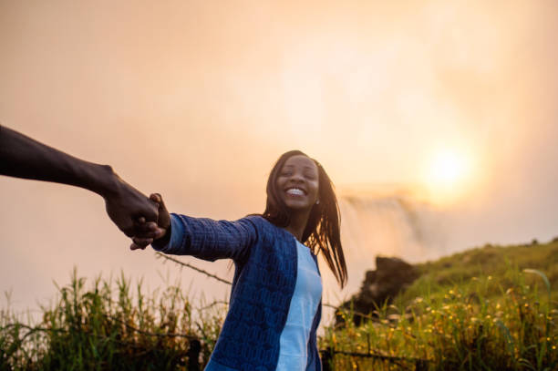 istock Looking over shoulder holding hands with Victoria Falls background 952965524