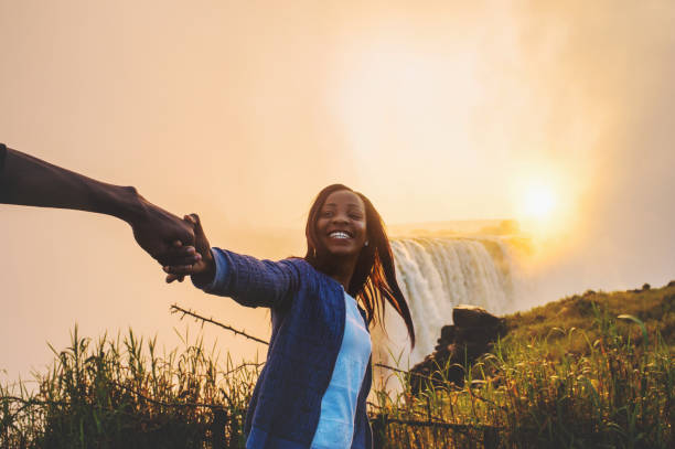 Looking and holding hands pulling towards Victoria Falls A personal perspective of a smiling happy woman leading and pulling someone excitedly towards Victoria Falls Zimbabwe Southern Africa at sunrise reach destination stock pictures, royalty-free photos & images