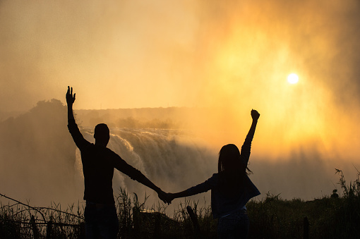 Silhouette of an African couple at the Victoria Falls Zimbabwe Southern Africa at a beautiful warm sunrise with spray in front of the rising sun