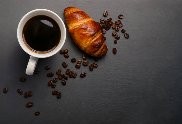 istock Fresh croissants and coffee and roasted beans on stone table. Top view with copy space. 952968890