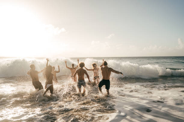 Exciting beach activities. Friends are waiting for the waves to hit their body. beach party stock pictures, royalty-free photos & images