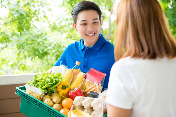 asian delivery man handing food over to a customer at her residence - polo shirt two people men working imagens e fotografias de stock