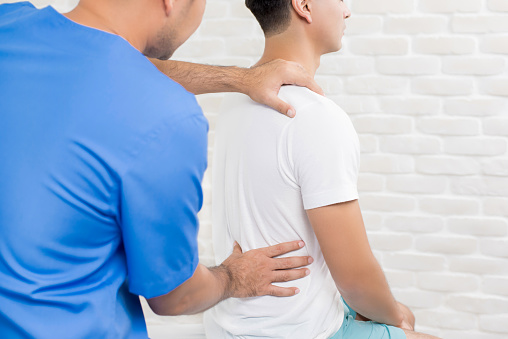 Male doctor therapist treating lower back pain patient in clinic or hospital - physical therapy concept