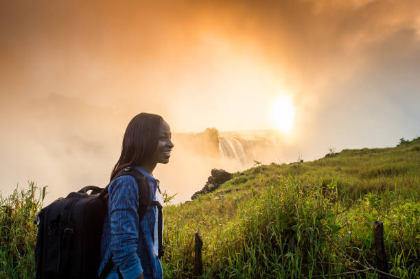 istock Woman with backpack looking at Victoria Falls at sunrise 952988240