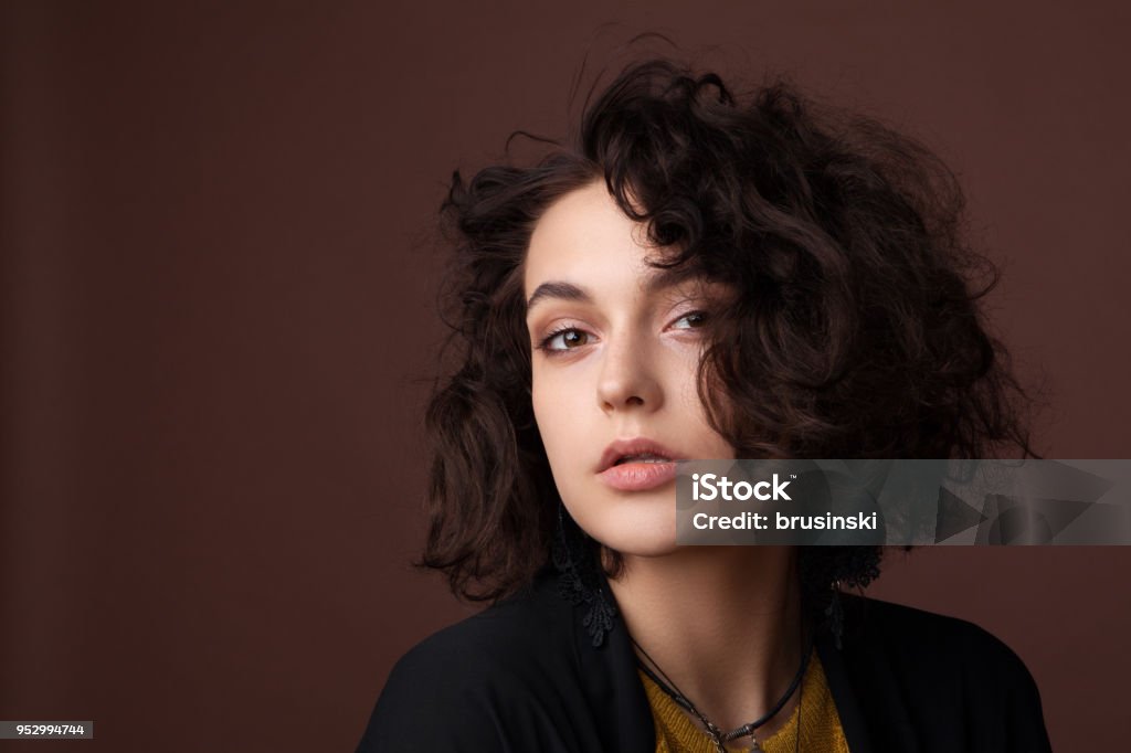 Close-up portrait of young beautiful girl in studio on brown background Close-up portrait of a young beautiful girl with curly hair in studio on a brown background Alternative Lifestyle Stock Photo