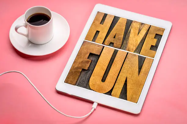 have fun word abstract - text in vintage letterpress wood type blocks on a digital tablet with a cup of coffee