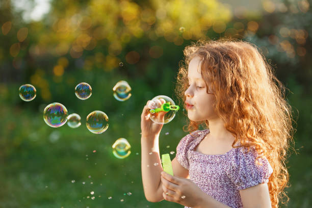 istock Little girl blowing soap bubbles in summer park. 953001490
