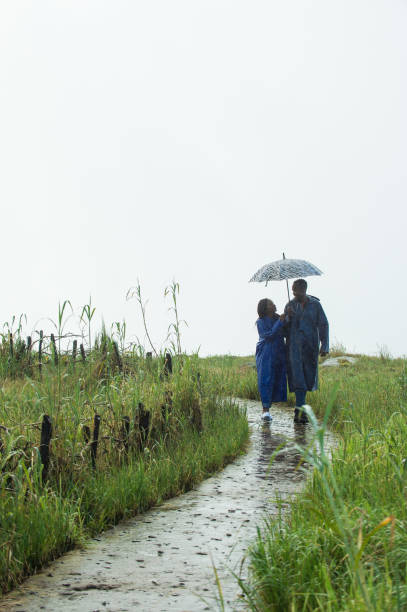 istock Couple walking together in Rain with rain coats and Umbrella on a path distant 953002634