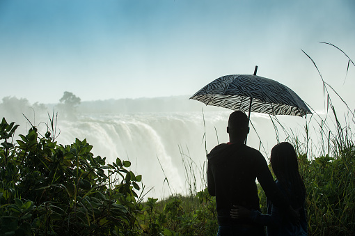 Silhouette of a couple standing together under an umbrella looking at Victoria Falls Mosi-oa-Tunya at sunrise Zimbabwe Africa