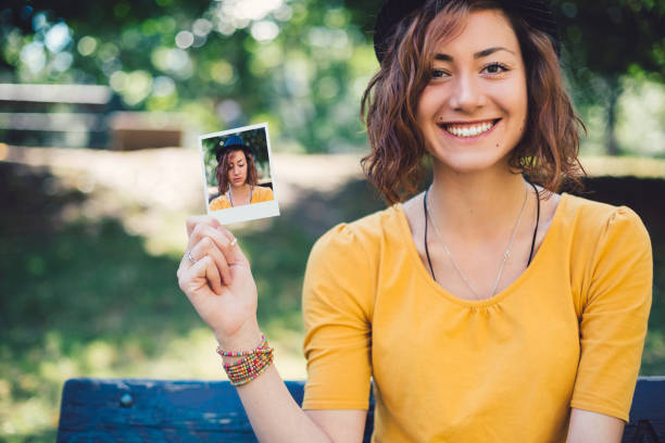 mujer sonriente mostrando selfie polaroid a la cámara - agarrar fotos fotografías e imágenes de stock