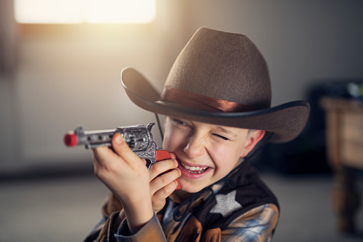 Little boy dressed up as cowboy playing with toy pistol.\nNikon D850