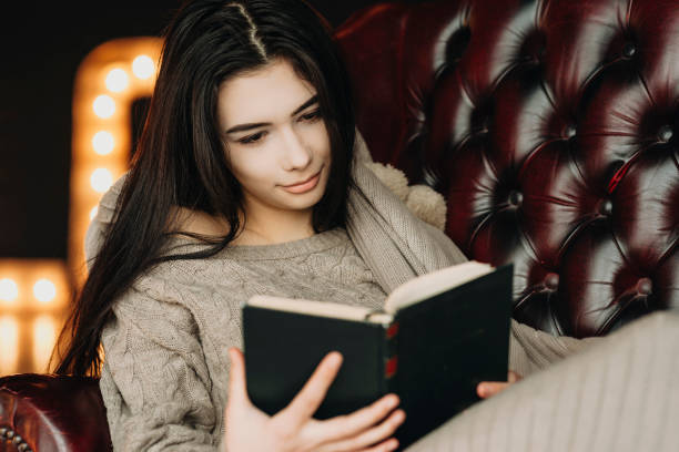 istock Cute young brunette sitting in a leather chair and reading a book. 953018006