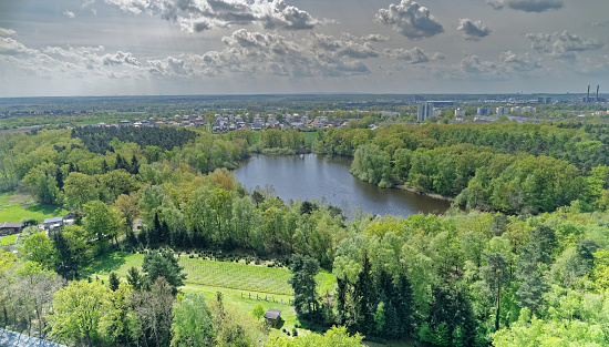 Aerial view of a small lake in the middle of the forest behind the industrial facilities of the city