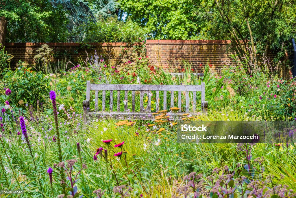 English Garden with wooden bench and wildflowers Lovely English Garden on a summer day with a wooden bench surrounded by wildflowers and trees Formal Garden Stock Photo