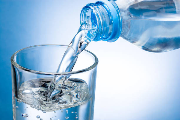 istock Pouring water from bottle into glass on blue background 953036212