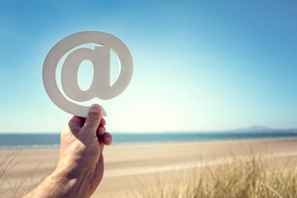 Email at symbol held up at the beach with copy space summer background