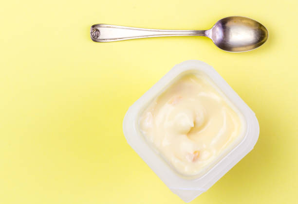 istock Yoghurt in cup on yellow background with small silver spoon 953039622