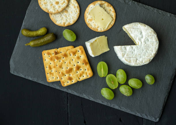 istock Cheese board with brie, grapes, pickles and crackers on black slate background 953039634