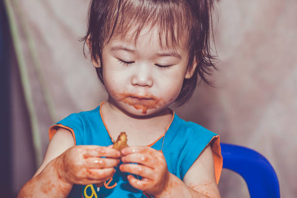Portrait of a asian child enjoy eating. Her hand and mouth get stained with ketchup and dirty. Charming girl playing with food and learning to eat. Do it yourself concept.